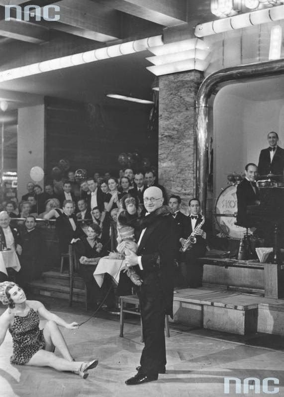 Franciszek Moszkowicz, kierownik i współwłaściciel Adrii, z szympansem na sali. Na drugim planie — orkiestra na estradzie. Fot. Narodowe Archiwum Cyfrowe.