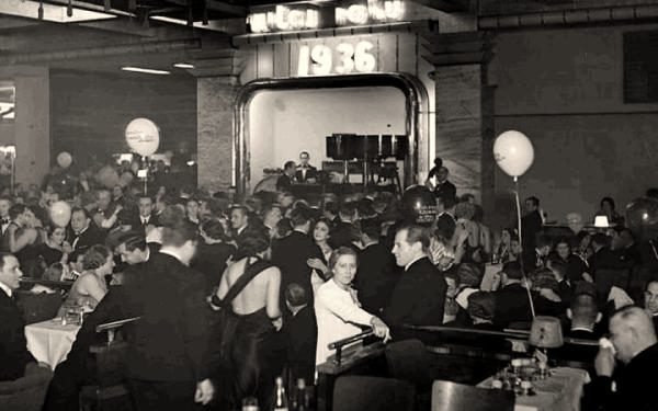 Bal sylwestrowy w Adrii — nad wejściem na salę świetlny napis „1936”; balony nad stolikami, w głębi orkiestra na estradzie. Fot. Narodowe Archiwum Cyfrowe.