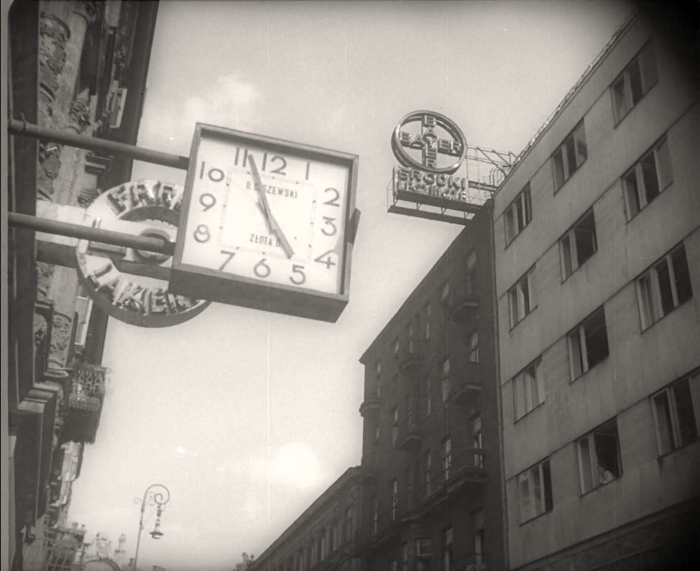 Złota Street just before W-Hour, 1 August 1944. The street clock shows five to five; on the right the Złota 7/9 building with the Bayer neon on the attic. A film frame from the collection of the National Film Archive.