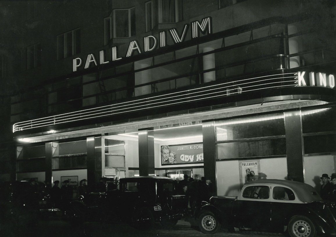 The Palladium cinema shortly after its opening, 1937: the neon signs above the marquee in full glow, on the poster „Maytime" with Jeanette MacDonald, cars and audience before the entrance. From the project's collection.
