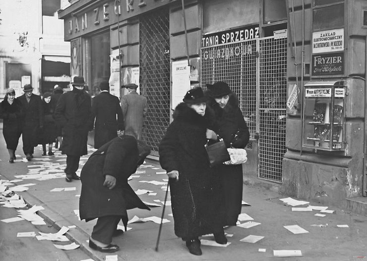 Nowy Świat przy Foksal, 18 grudnia 1938 — dzień wyborów do Rady
Miejskiej. Salon Jana Zegrze za opuszczoną kratą, chodnik zasłany
ulotkami wyborczymi; obok tablica „Tania sprzedaż gwiazdkowa”, szyldy
Zakładu Elektromechanicznego „M. Chotkowski i W. Kozicki” oraz fryzjera
damskiego „Józef Kobyłecki”.
