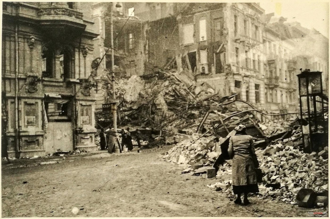 Nowy Świat od strony Foksal, jesień 1939, przed odgruzowaniem:
zwały cegieł i belek sięgają środka jezdni, kobieta w płaszczu wspina
się po gruzie; po lewej ocalała część kamienicy, w głębi wypatroszony
narożnik. fotopolska.eu.